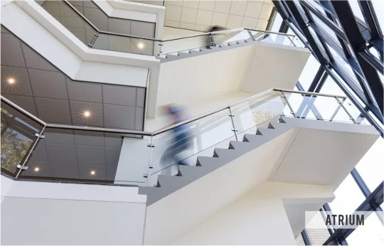 Moderne trappenhal in het Atrium-gebouw aan de Baarnsche Dijk met glaswanden en bewegende personen.